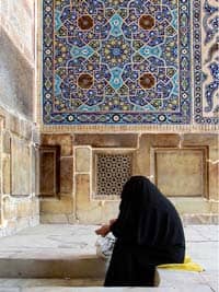 Source: http://www.flickr.com/photos/hamed/196805560/ Title: woman in black chador prays on steps of mosque, blue tiled decorations in background